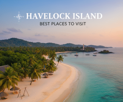 Aerial sunset view of a pristine white-sand beach with palm trees and a few thatched umbrellas on Havelock Island. The turquoise water meets the shore, with small boats anchored offshore and a red and white lighthouse visible in the distance on a small peninsula. The text 'HAVELOCK ISLAND BEST PLACES TO VISIT' is overlaid on the image, along with a simple compass rose.